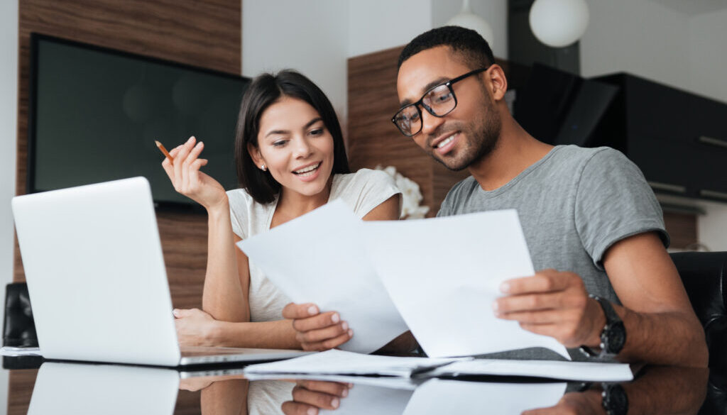 Cheerful loving young couple using laptop and analyzing finances