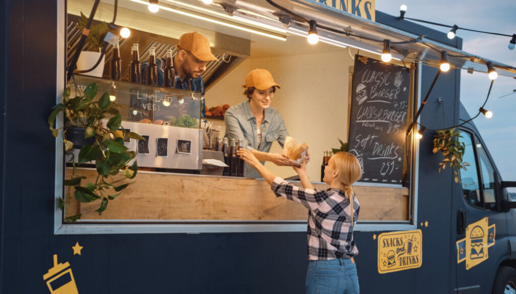 Food Truck Employee Hands Out a Freshly Made Burger and a Soft Drink to a Happy Young Female. Street Food Truck Selling Burgers in a Modern Hip Neighbourhood